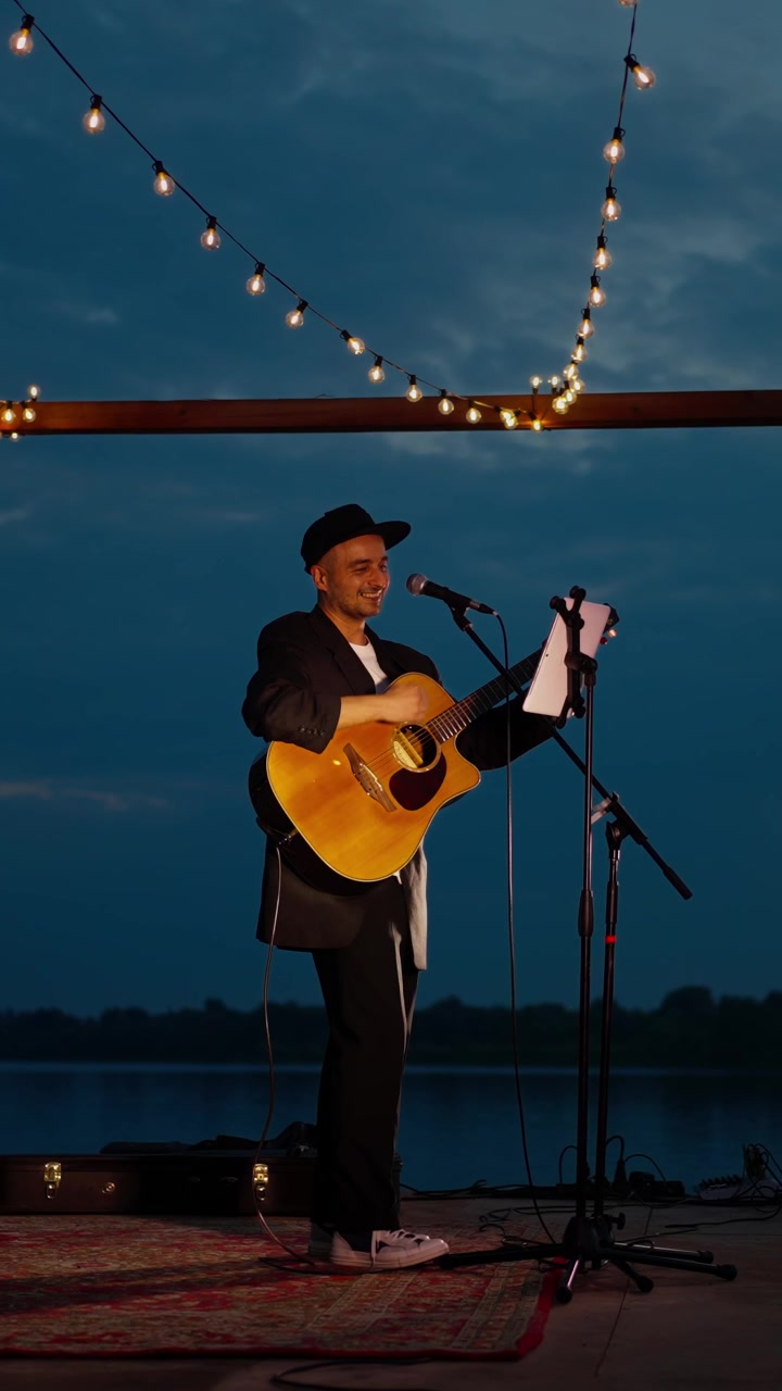 Musiker fremfører akustisk gitar og sang på utendørs scene i skumringen