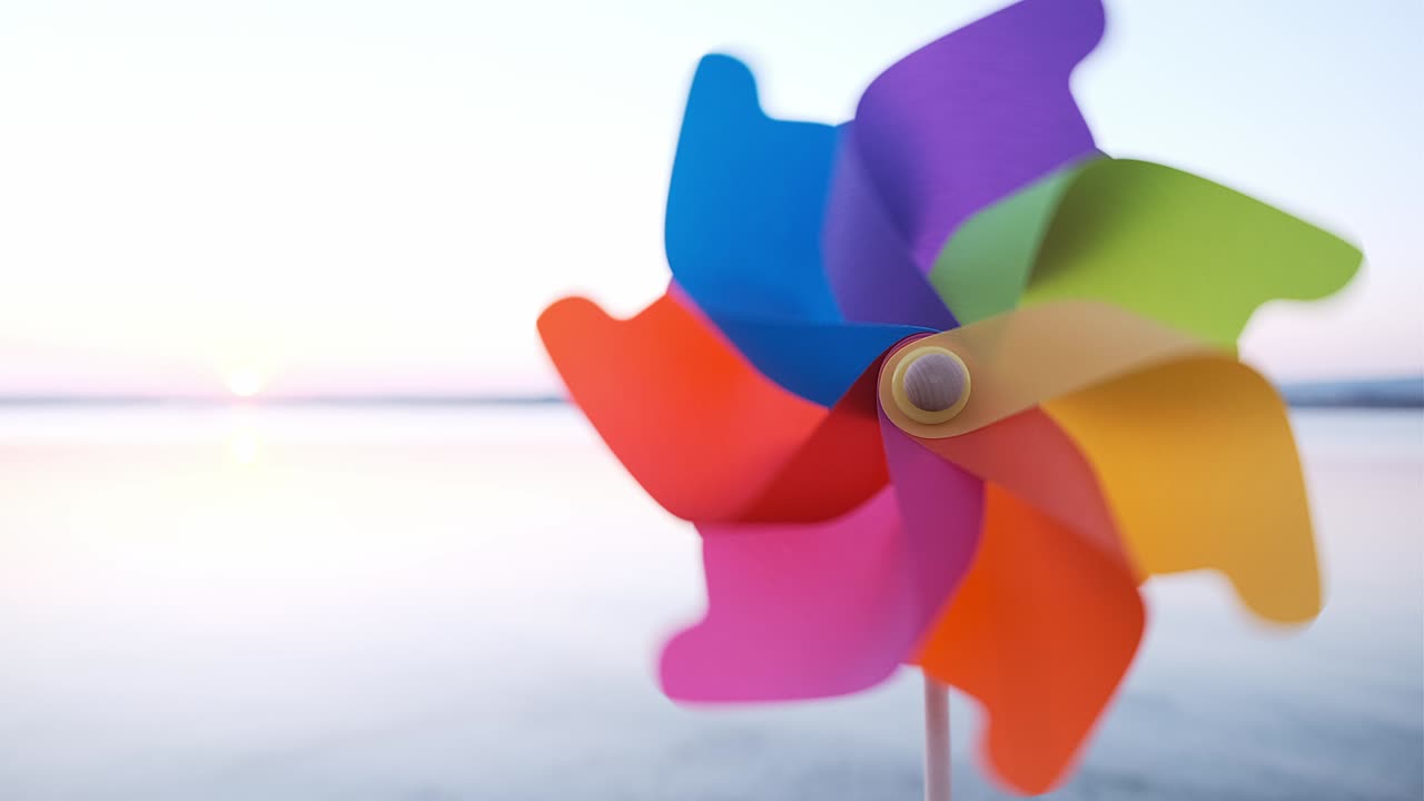 플라스틱의 핀을 회전시켜 바람이 불면서 바다의 부드러운 표면과 밝은 분홍색 해가 지는 바다의 모래 위에 서 있습니다. 해변에 장난감 공장. 태양의 큰 디스크.