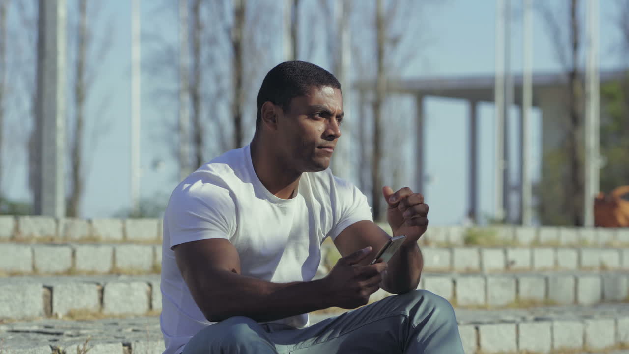 hombre pensativo mirando el teléfono y sosteniendo la mano en la barbilla.