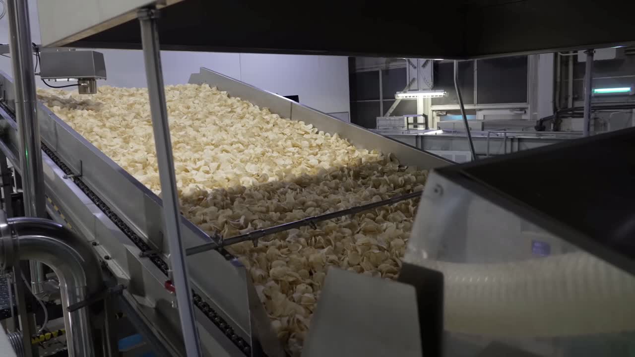 Close up shot chips are fried and poured into the packaging process