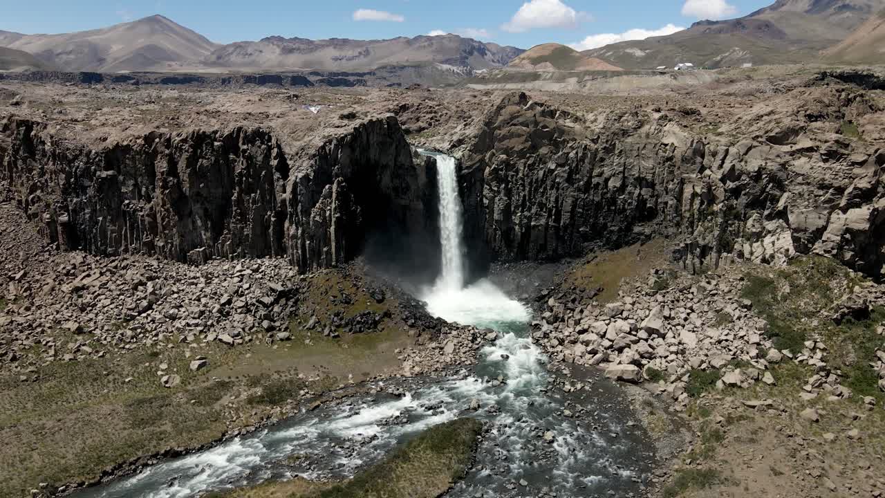 Aerial orbit of the Maule waterfall with its powerful riverbed and the arid mountains of this region of Chile in the background on a sunny day