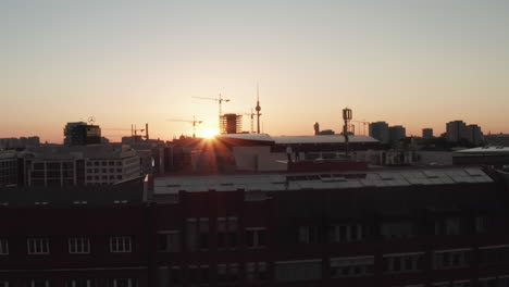 Confident-Young-Man,-Guy-standing-on-rooftop-in-Golden-Hour-light-with-Urban-Skyline-of-Berlin,-Germany-and-Beautiful-Sunlight-and-Summer-Vibe,-Aerial-Establishing-Shot