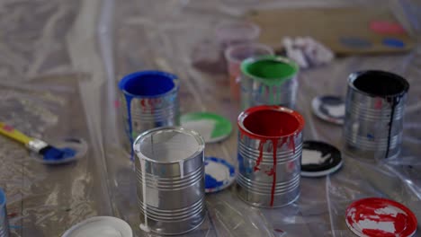 Overview-of-paint-cans-on-floor-at-industry,-high-angle-circling-shot-of-containers-at-workshop