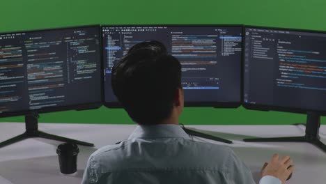 back view of asian man developer having headache while write code with multiple computer screens in green screen studio