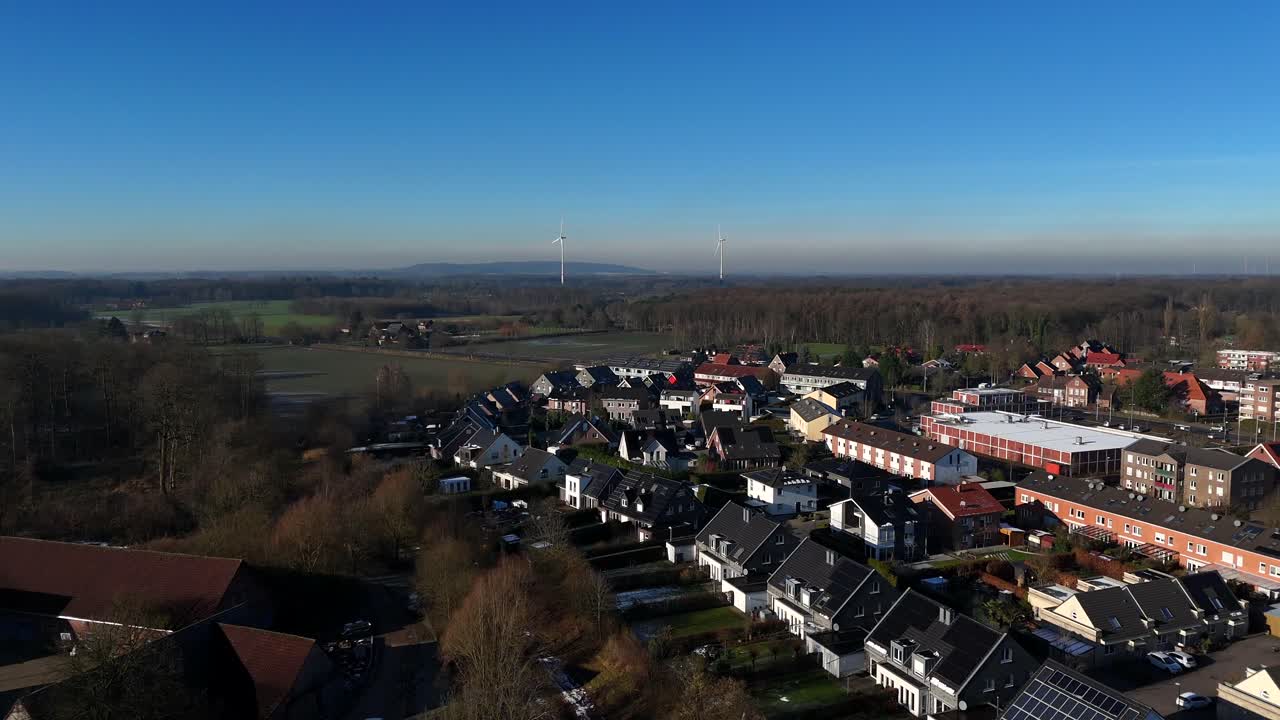 Luxury homes in small town during golden sunrise. Blue sky and wind turbines in distance. Historic farmstead in countryside. Aerial forward wide shot.
