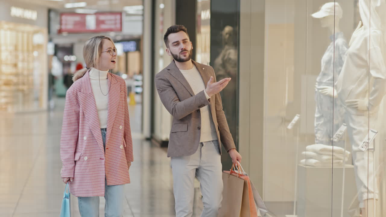 Trendy Couple Walking Along Mall Shopping For Clothes