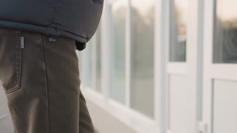 close up side view of man in dark jacket and olive pants walking outdoors, hand relaxed at side, with blurred urban background and soft daylight creating casual and natural street atmosphere