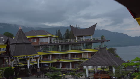 Pan-shot-of-traditional-Indonesian-resort-with-mountains-and-fog-in-the-background-on-Lake-Tabo-island-Samosir,-North-Sumatra