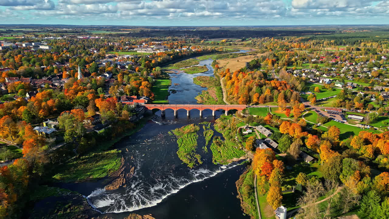 Kuldiga Brick Bridge Over Venta River Near Ventas Rumba Waterfall During Autumn In Kuldiga, Latvia. aerial pullback shot