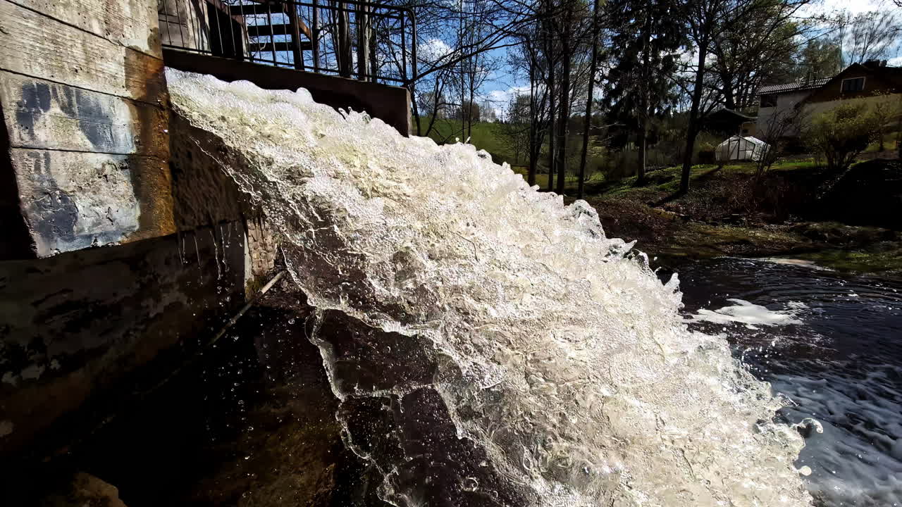 Waterfall water rushes from dam structure in creating foamy cascade