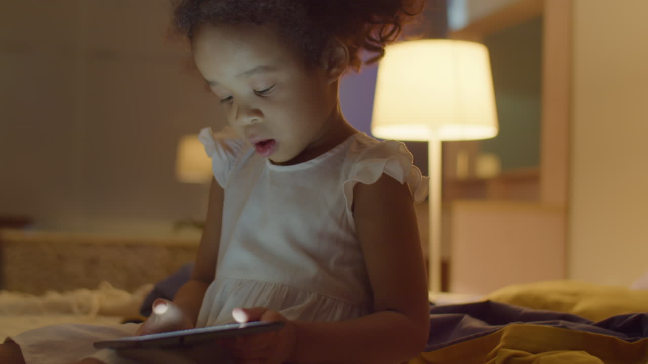 Little Asian Girl Playing on Tablet in Evening at Home