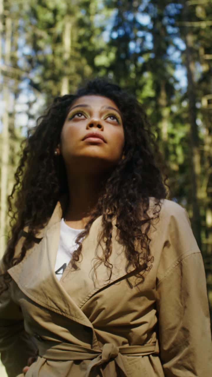 Woman with curly hair in a forest wearing a trench coat