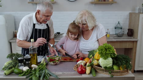 Senior-couple-in-kitchen-teaching-granddaughter-child-how-to-cook,-chopping-pepper-with-knife