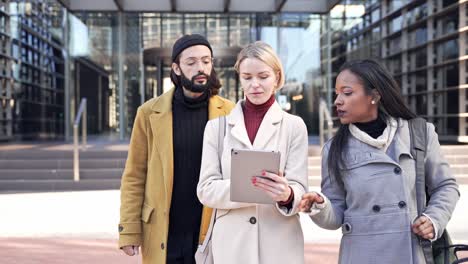 three business coworkers talking about project, using digital tablet and walking outside the office