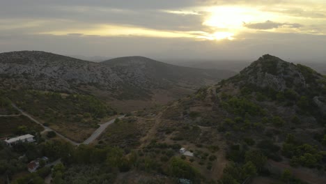 Drone-aerial-view-of-a-car-passing-on-a-countryside-road-with-mountains-and-sunset