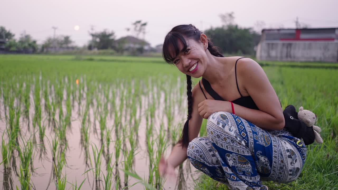 Smiling Woman Crouching in a Green Rice Field
