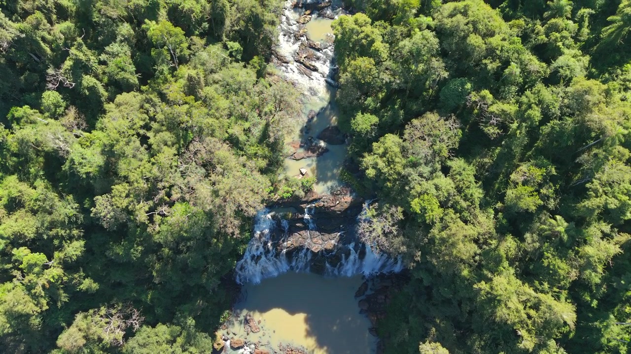 Cascata a più livelli circondata dalla fitta Foresta Atlantica dell'Alto Paraná vicino al Lago Urugua-i, Misiones, Argentina, che evidenzia la foresta pluviale subtropicale incontaminata, ripresa aerea con drone dall'alto in avanti