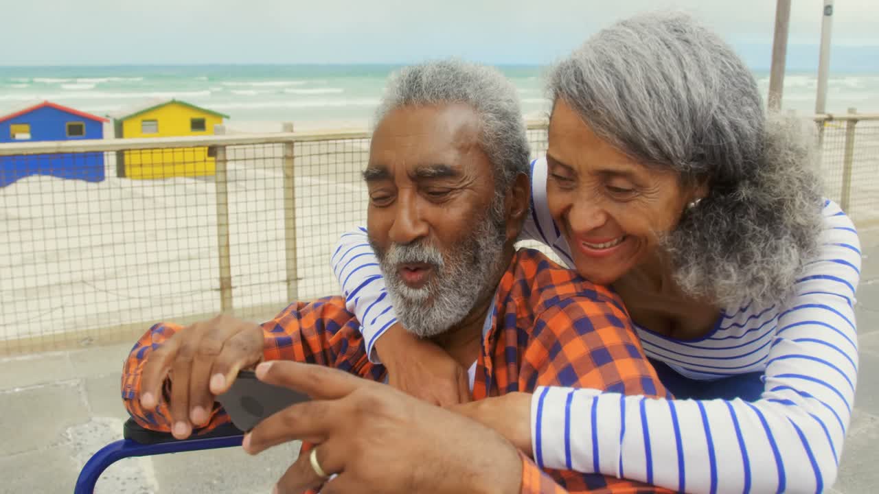 Front view of active senior African American couple taking selfie with mobile phone on promenade 4k