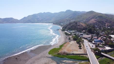 Aerial-view-rising-over-coastal-road-between-ocean-and-rugged-mountains-in-capital-city-of-Dili,-Timor-Leste,-Southeast-Asia