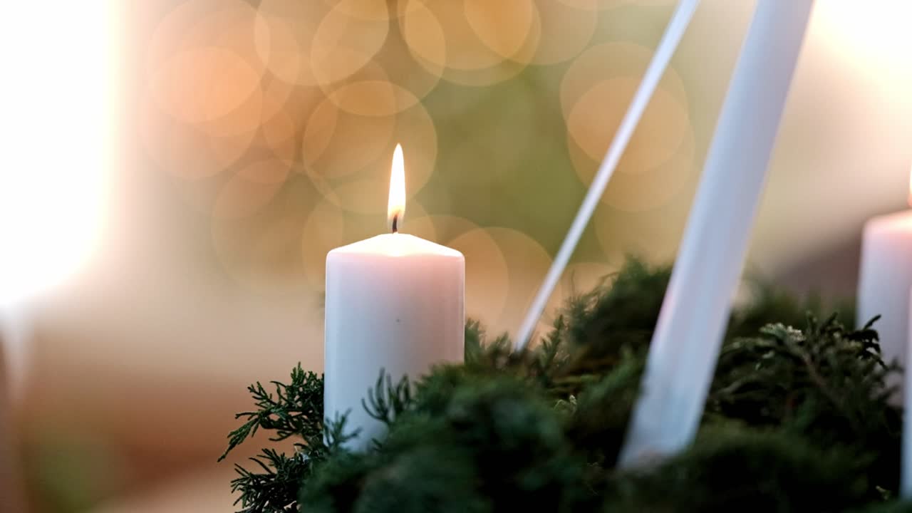 Candela dell'avvento bianca accesa su una ghirlanda con un albero di Natale sullo sfondo