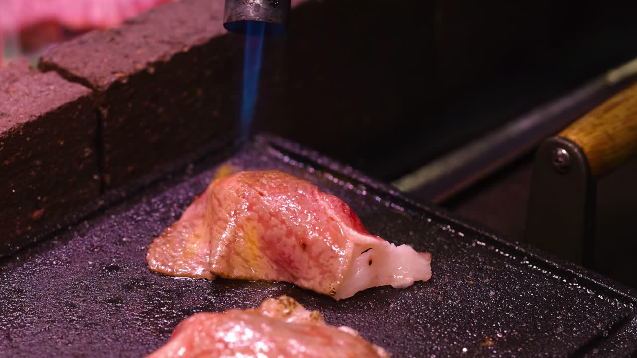 A close-up view of a steak being seared with a torch on a griddle.