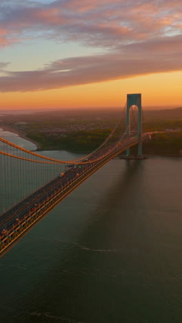 Light of setting sun falling on the supports of Whitestone bridge. Beautiful scenery of the river and Bronx at pink sky backdrop. Vertical video