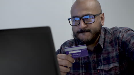 un primer plano de un hombre indio contemplando su decisión de comprar un producto caro en línea usando su tarjeta de crédito