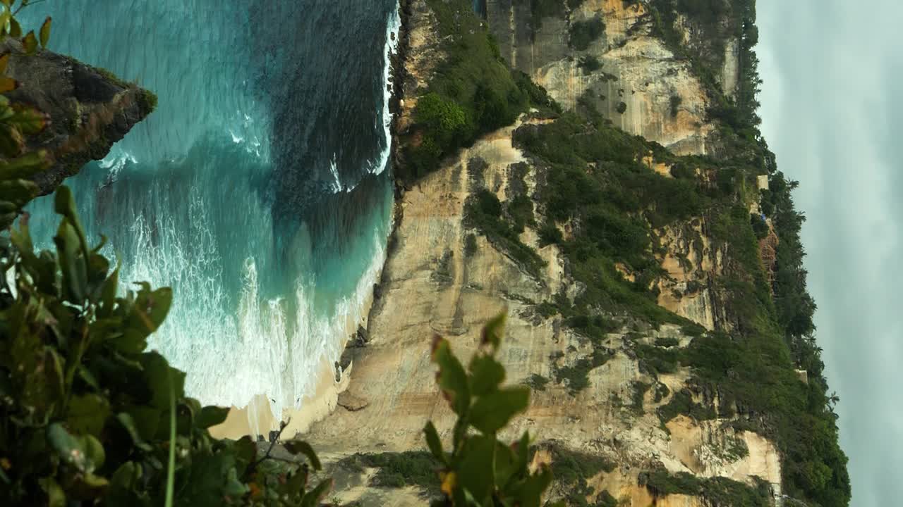tomada vertical de los acantilados de nusa penida en bali, indonesia con vistas al mar azul con olas en la playa de diamantes y acantilados en una hermosa mañana