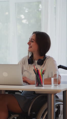 mujeres alegres sonriendo dando los cinco altos después de completar la tarea. estudiante con discapacidad en silla de ruedas utiliza la computadora portátil mientras la amiga hace notas en el bloc de notas