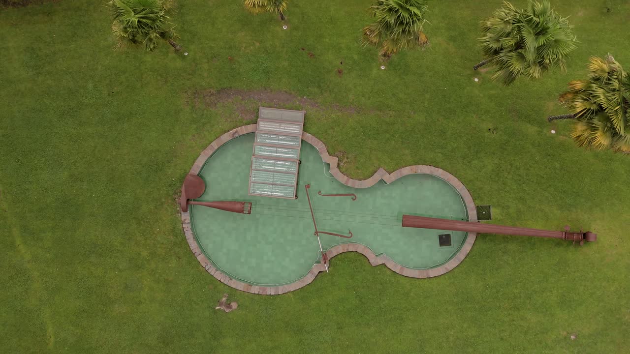 Aerial view of a violin-shaped water feature in a park surrounded by greenery