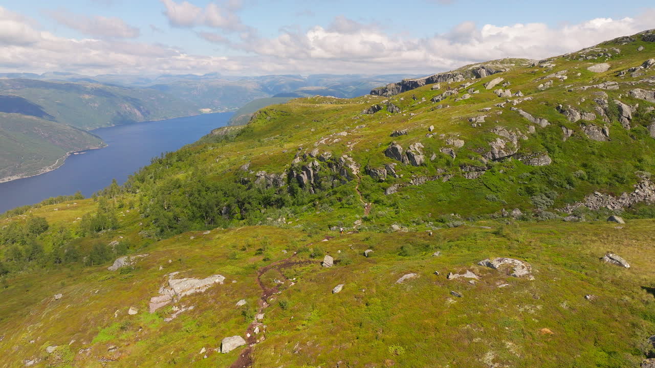 Vandrere på bjergsti med udsigt over sø i et episk landskab, Norge
