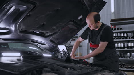 a male auto repairman in a car service with a computer checks the hood of the car