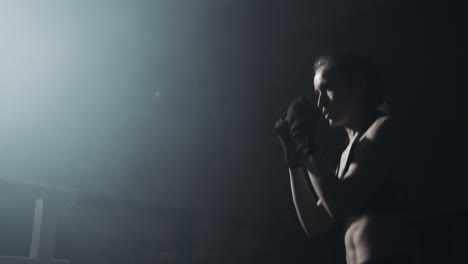 a female boxer training in a dark, smoky gym with a spotlight