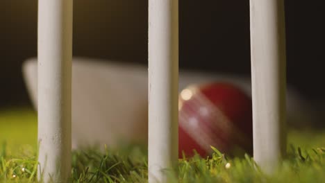 Cricket-Stillleben-Mit-Nahaufnahme-Von-Ball-Und-Schläger,-Die-Im-Gras-Hinter-Stümpfen-Liegen-3