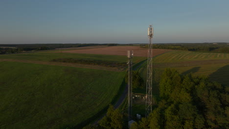 two radio towers in the middle of farmland during sunrise, aerial orbital dolly in tilting