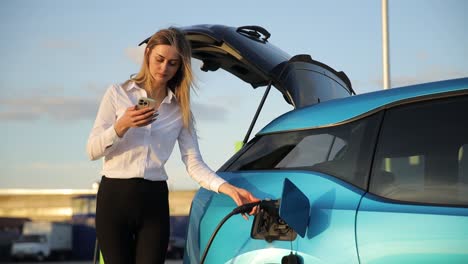 a woman charges her electric car while checking updates on her phone, highlighting the convenience of electric vehicles and technology in transportation