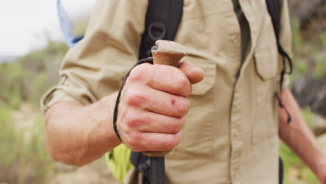 midsection of caucasian male survivalist trekking through wilderness with backpack and walking poles