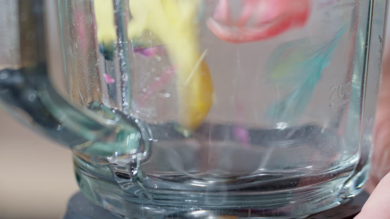 Camera outside glass blender as rotating blades shatter plastic into tiny pieces, symbolizing toxic pollution