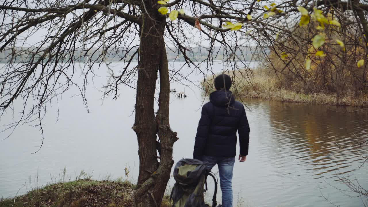 Man standing near river. Young man with backpack walking near the river in autumn season
