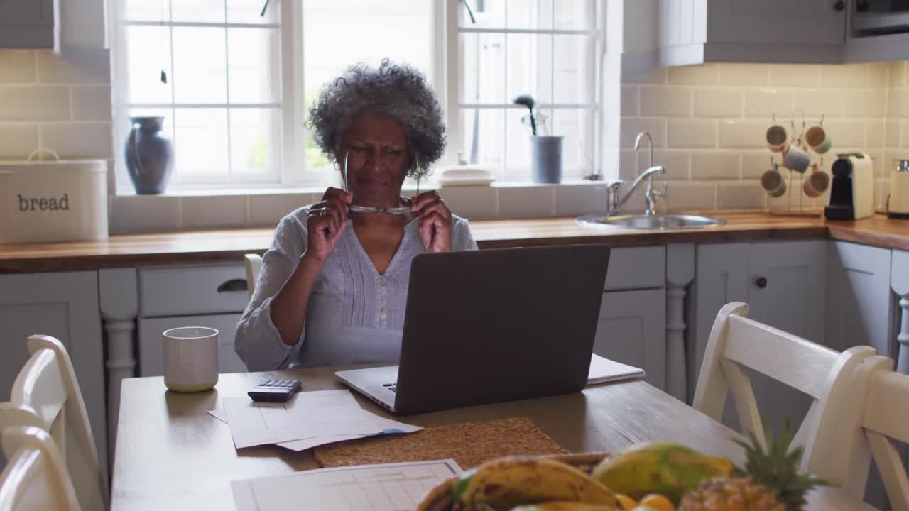 Stressed senior african american woman using laptop and calculating finances at home