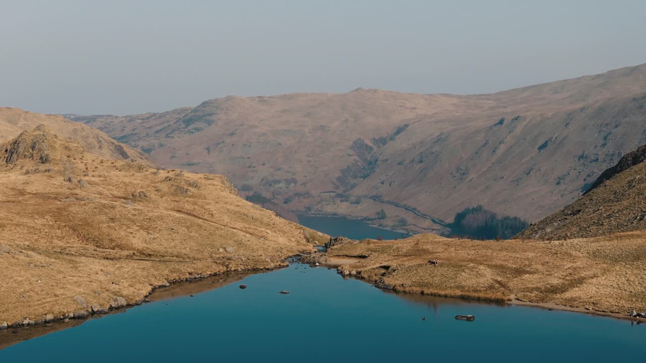 Ascending pan down over mountaintop lake in Lake District revealing valley below