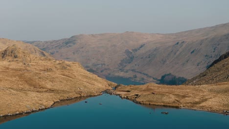 ascending pan down over mountaintop lake in lake district revealing valley below