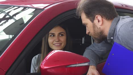 mujer atractiva sentada en un coche nuevo hablando con el vendedor