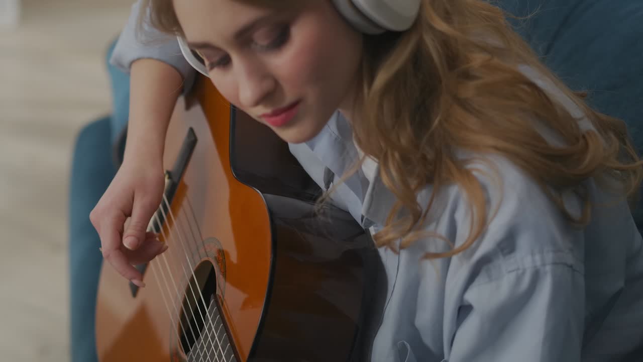 young woman is making music, playing guitar in apartment, looking at green screen of laptop, chroma key technology