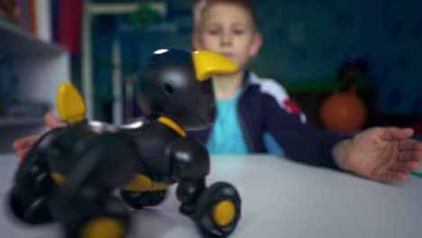 a game with a robot dog. sad child dreams of a puppy. a boy sits at a table with a toy dog.