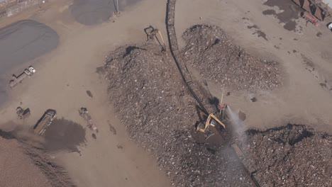 aerial view of scrap handling with excavators, conveyor system, and active dust suppression.
