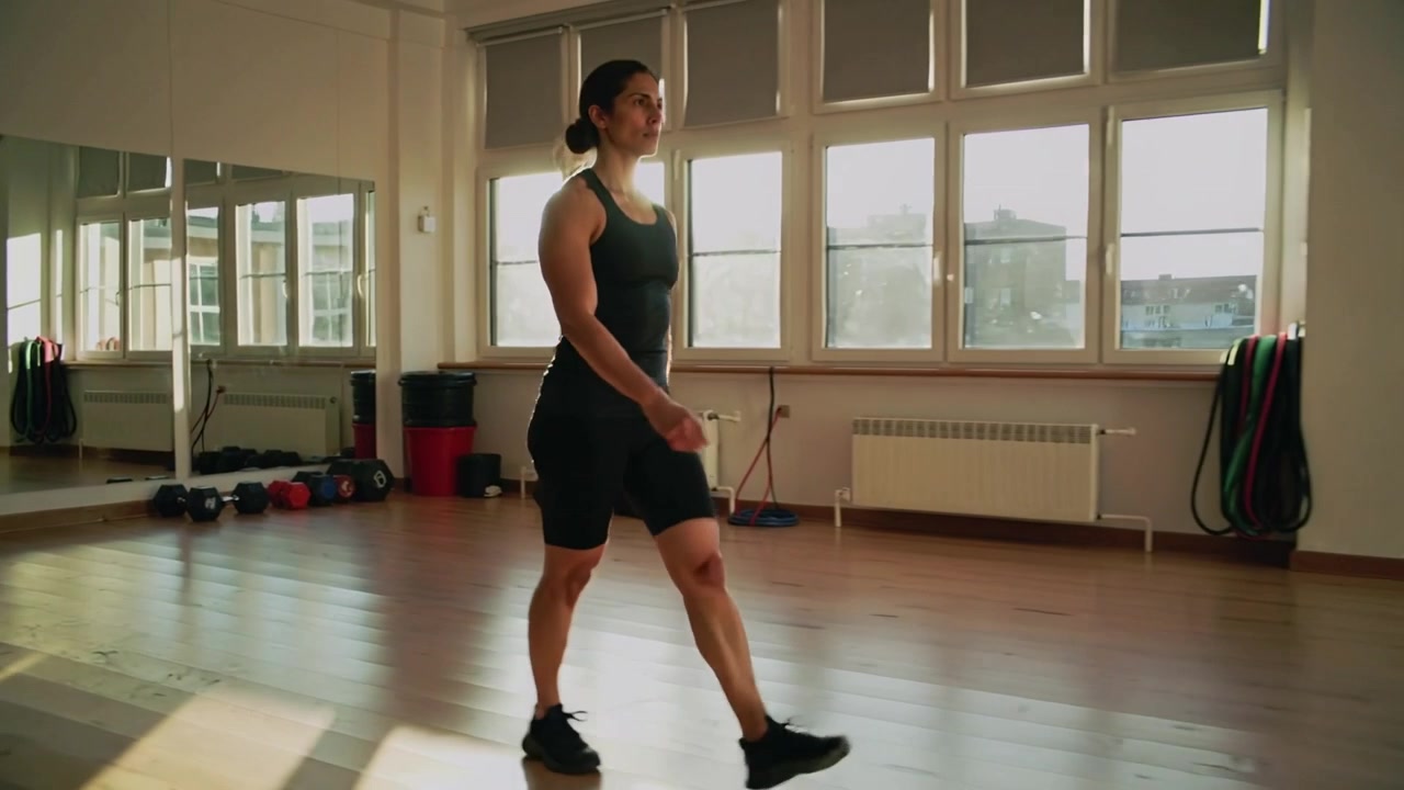 Donna che cammina dopo il segnale, facendo passi costanti attraverso la palestra in abbigliamento da allenamento nero con specchio e pesi.