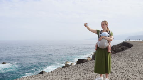 junto al mar en un día de verano, una madre y su bebé crean momentos preciados al aire libre. el niño descansa cómodamente en una mochila de canguro durante su caminata