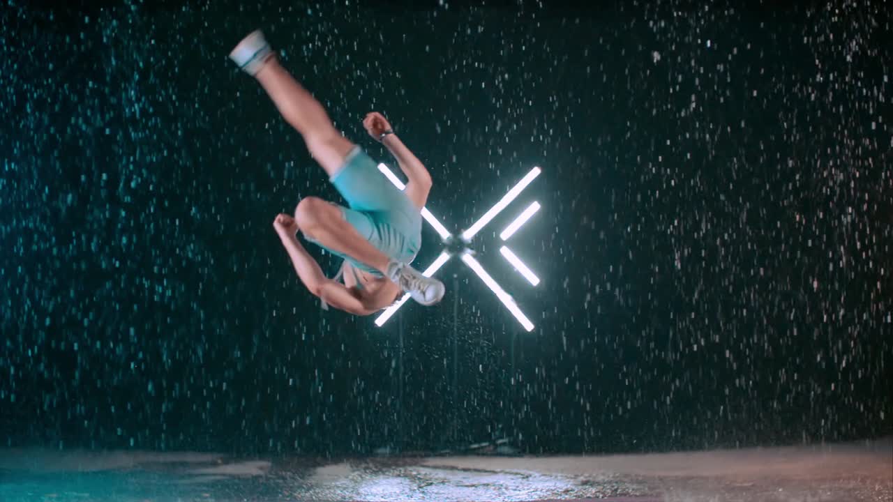 Incredible martial arts spinning flip kick tricking by caucasian male in rain, slow motion