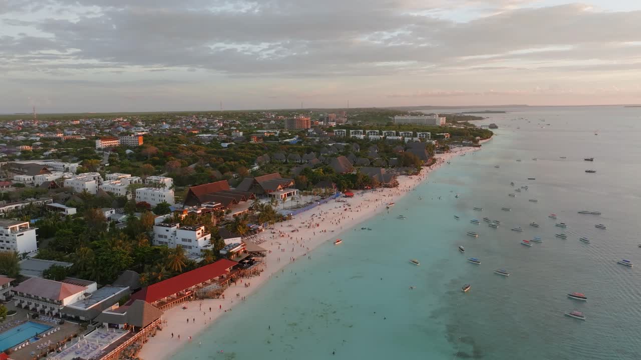 Zanzibar'da gün batımında Nungwi Halk Plajı üzerinde sinematik, ileriye doğru hareket eden drone çekimi. Altın rengi gökyüzü, sakin okyanus ve tropikal sahil şeridi, turizm projesi için ideal, huzurlu ve çarpıcı bir seyahat sahnesi oluşturuyor